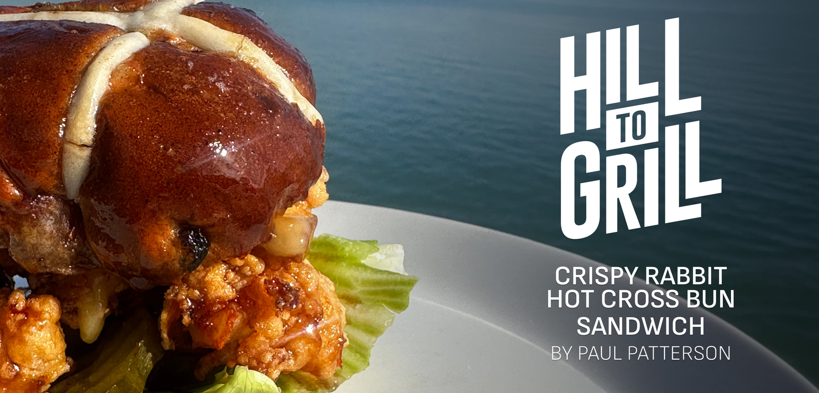 Crispy rabbit hot cross bun sandwich on a plate with 'Hill to Grill' branding.