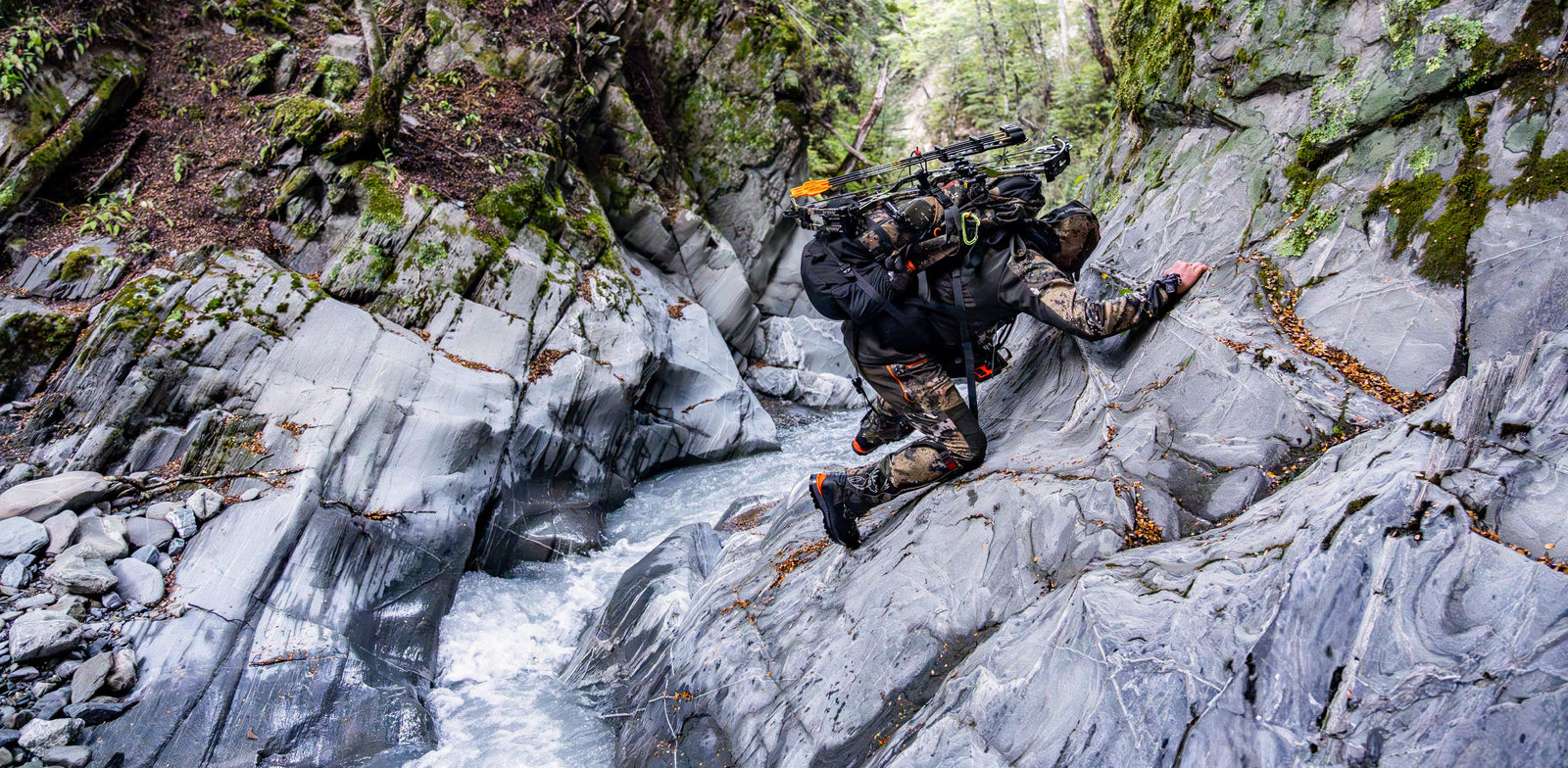 Person with a backpack climbing rocky terrain next to a stream