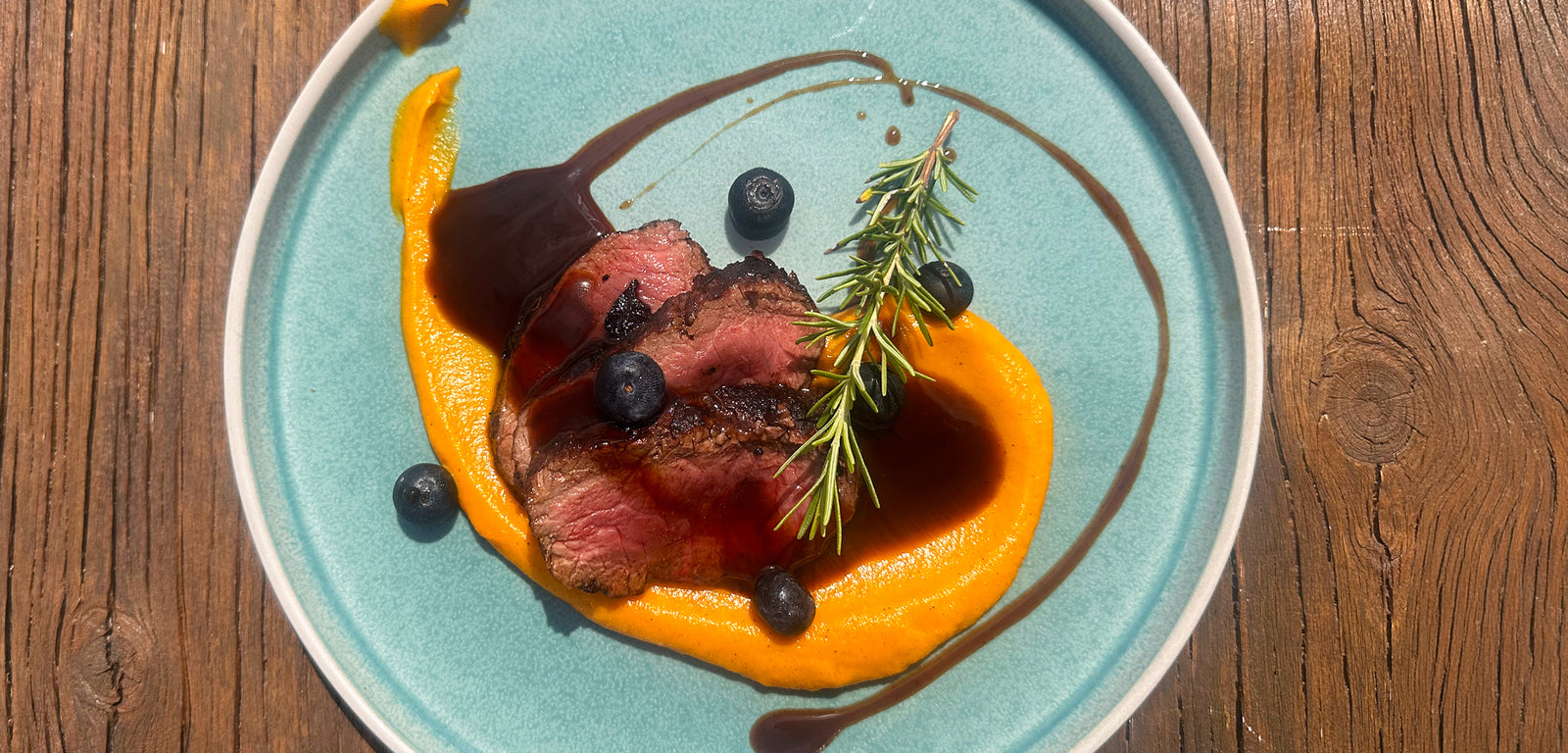 Plated dish with beef, orange, blueberries, and a drizzle of sauce on a wooden table.