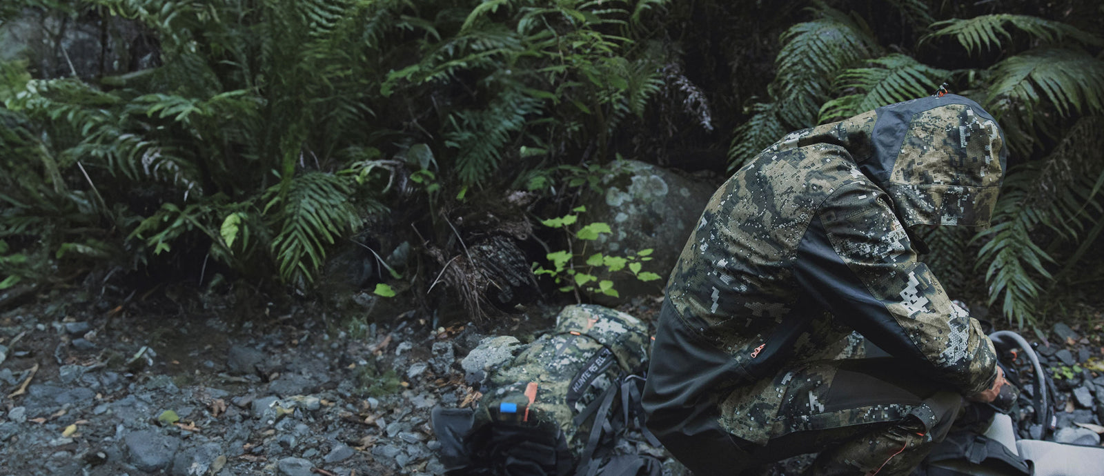 Person in camouflage gear sitting on the ground in a forest setting